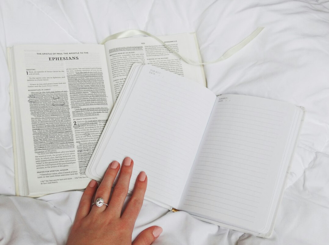 Hands writing in a paper journal next to a laptop and coffee cup